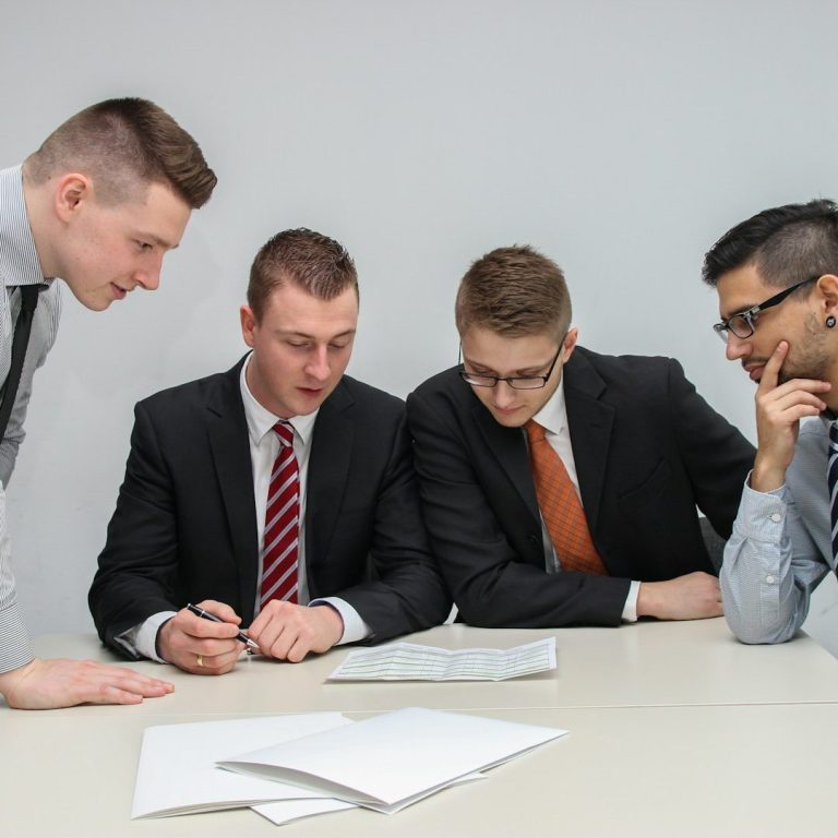 Cuatro hombres de negocios discutiendo y revisando documentos en una mesa.
